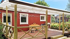 A red wooden building with a covered patio area, a wooden table, and chairs. - 5 Person Holiday Home in Billingfors (Billingsfors)