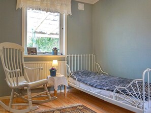 Et værelse med en enkeltseng, en gyngestol, et lille bord med en lampe og et vindue med udsigt til grønne omgivelser.