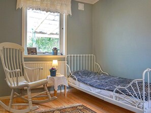 A room with a single bed, a rocking chair, a small table with a lamp, and a window with a view of greenery. - 5 Person Holiday Home in Billingfors (Billingsfors)