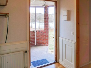 En døråbning der fører ud til en balkon med en murstensvæg og en hvid dør med lyskontakt.