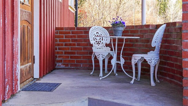 A patio with a white metal table and chairs, a potted plant, and a red brick wall. - 5 Person Holiday Home in Billingfors (Billingsfors)