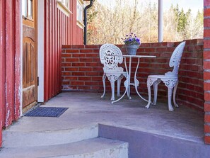A patio with a white metal table and chairs, a potted plant, and a red brick wall. - 5 Person Holiday Home in Billingfors (Billingsfors)