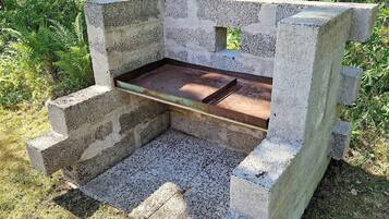 A concrete bench with a metal tray, surrounded by grass and plants.