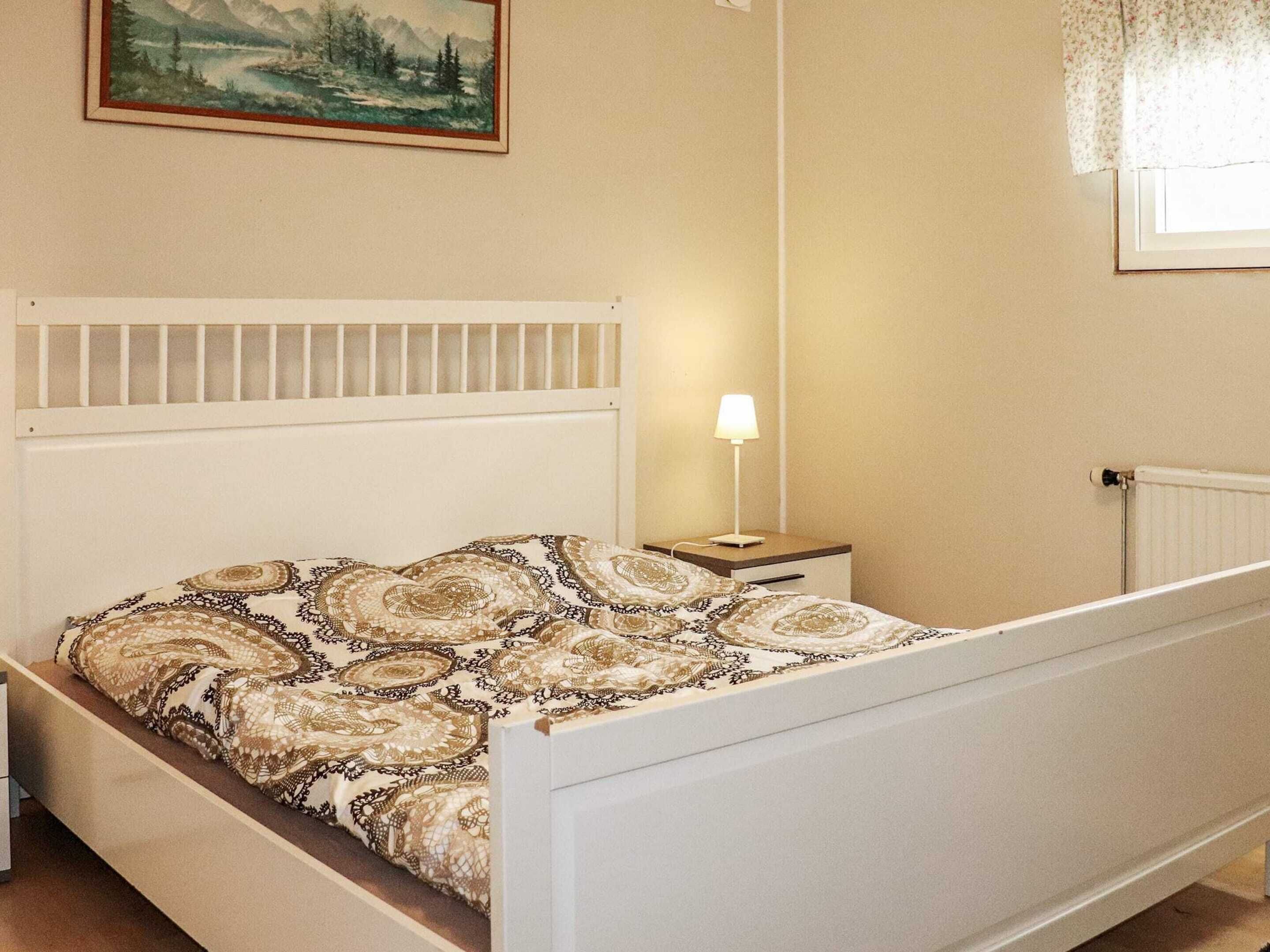 A bedroom with a bed, a nightstand, a lamp, a radiator, and a painting on the wall.
