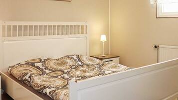 A bedroom with a bed, a nightstand, a lamp, a radiator, and a painting on the wall.