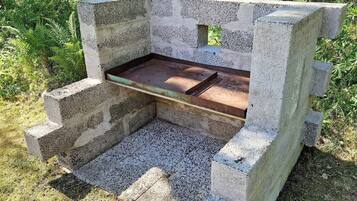 A concrete bench with a metal tray, surrounded by grass and plants.