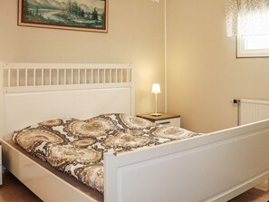 Un dormitorio con cama, mesita de noche, lámpara, radiador y un cuadro enmarcado en la pared.