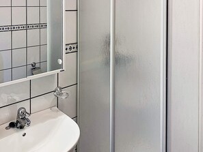 Un baño con lavamanos blanco, espejo y mampara de ducha.