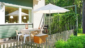 Een terras met een tafel, stoelen, een barbecue en een houten omheining.