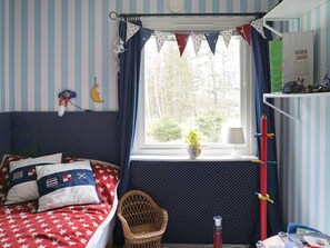 A bedroom with striped walls, a bed with a star-patterned blanket, a window with a view of trees, a wicker chair, and a shelf with items. - 4 Star Holiday Home in Ekero (Ekerö)