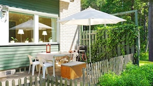 Een terras met een tafel, stoelen, een barbecue en een houten hek.