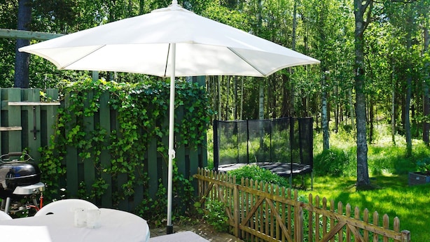 Een houten terras met een witte parasol, een barbecue en een trampoline.