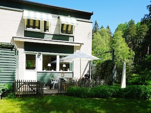 Ein zweistöckiges Gebäude mit Veranda, Sitzgelegenheiten im Freien und einem Holzzaun.
