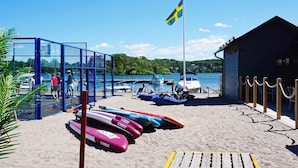 Een strand met een vlag, een blauwe constructie en diverse vaartuigen.