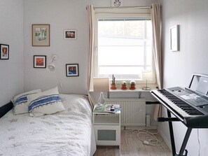 A bedroom with a bed, a window with curtains, a radiator, a keyboard, and wall decorations. - 4 Star Holiday Home in Ekero (Ekerö)