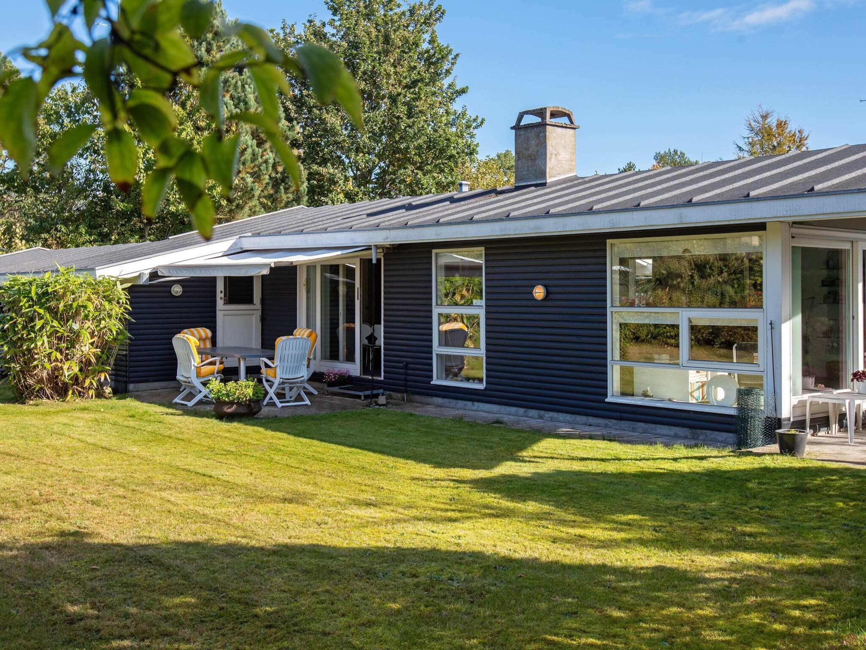A modern house with a dark exterior, a covered patio with outdoor furniture, and a well-maintained lawn.