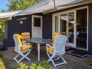 A cozy outdoor seating area with a table and two rocking chairs, a sliding glass door leading to an interior space, and a small step leading to the door. - Cozy Retreat in Marielyst - By Traum Ferienwohnungen (Vaeggerlose)