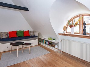 Un dormitorio acogedor en el ático, con techo inclinado, una banca empotrada con cojines, una mesita y una ventana con vistas al exterior.