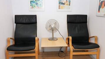 Två svarta läderstolar placerade mittemot varandra, med ett litet bord och en golvfläkt mellan dem.