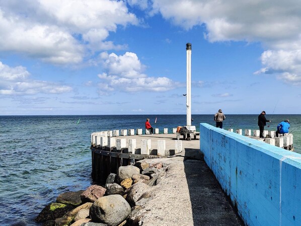 A pier with a lighthouse, rocky shore, and calm sea. - 6 Person Holiday Home in Hadsund (Hadsund)