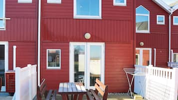 A red building with a white door, windows, and a small porch with a table and benches.