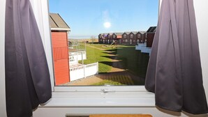 A room with a window overlooking a grassy area with a playground, a red building, and a row of houses. - 6 Person Holiday Home in Hadsund (Hadsund)