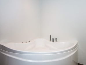 A white bathtub with a curved design, a single faucet, and a control knob.