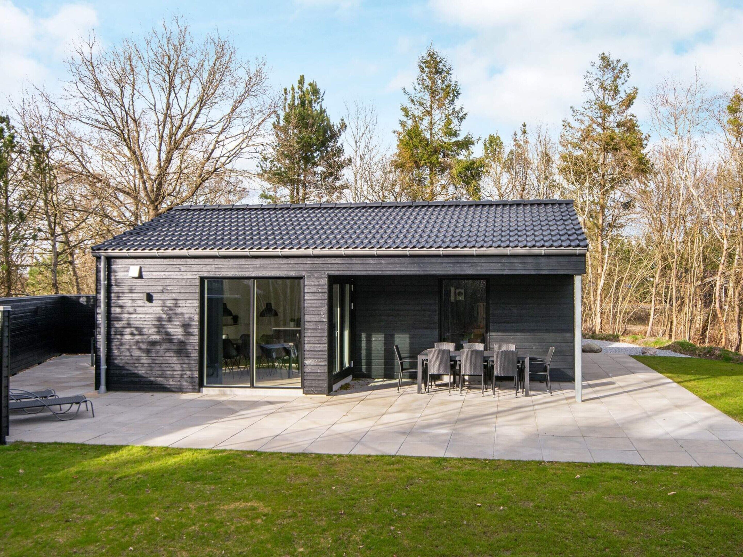 A modern house with a patio, large windows, and a tiled roof.