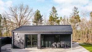 Une maison moderne dotée d’un patio, de grandes fenêtres et d’un toit recouvert de tuiles.