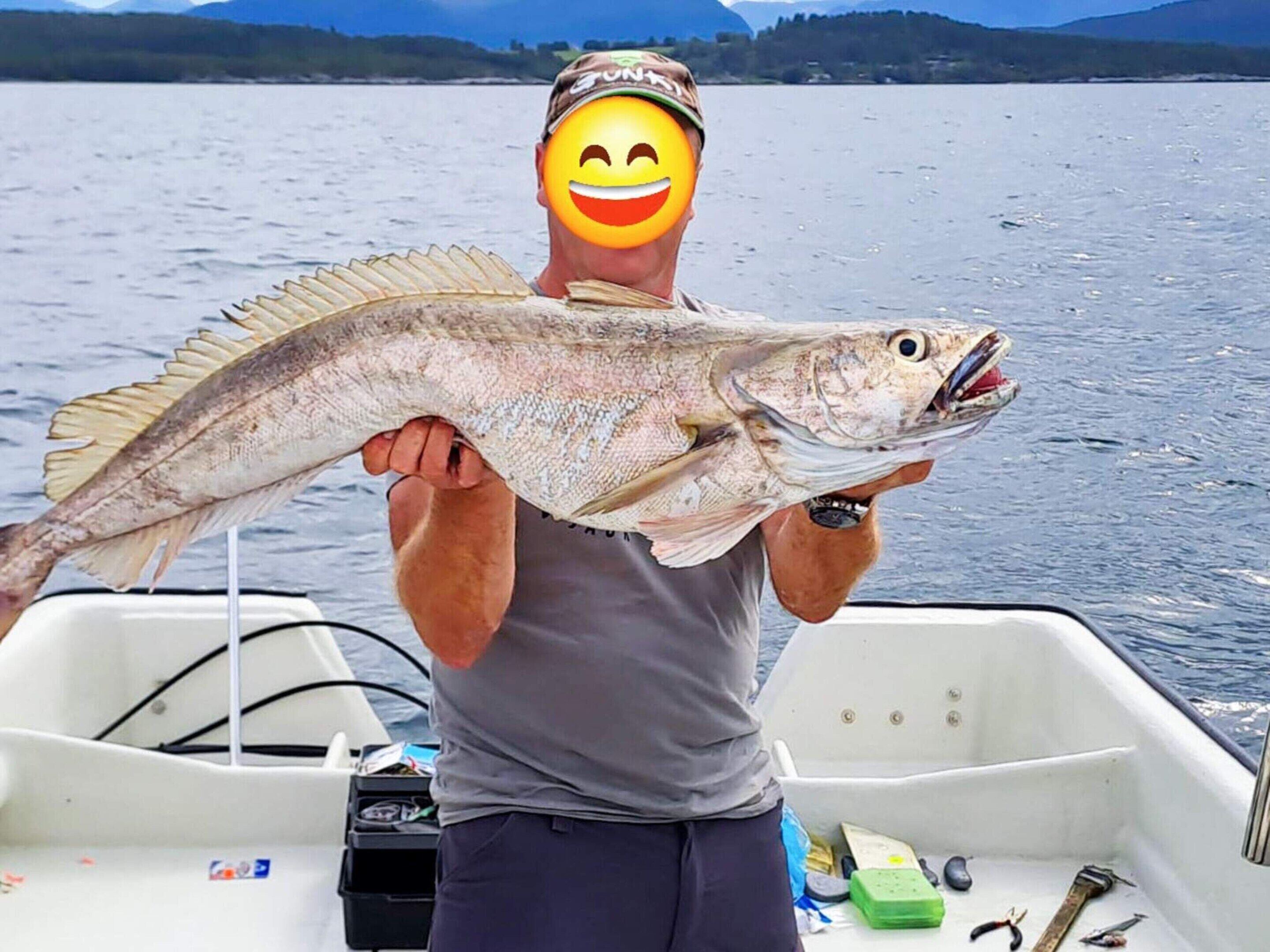 A person holding a fish on a boat with a calm lake and mountains in the background.