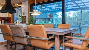 A modern dining area with a wooden table and four chairs, a hanging light fixture, and a view of the outdoors through large windows. - 8 Person Holiday Home in Kolind (Kolind)