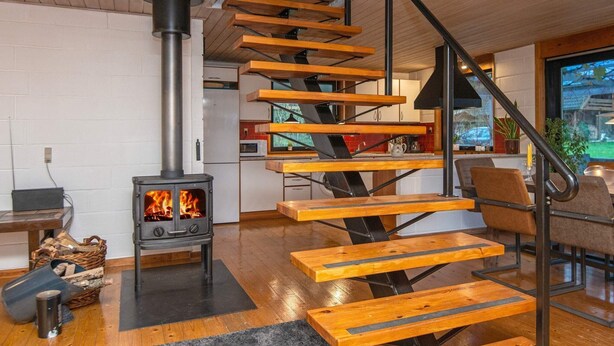 A modern interior with a wooden staircase, a wood-burning stove, and a kitchen area. - 8 Person Holiday Home in Kolind (Kolind)