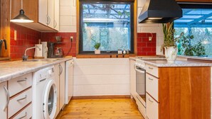 A modern kitchen with wooden cabinets, a built-in washing machine, a large window with a view of trees, and a black range hood. - 8 Person Holiday Home in Kolind (Kolind)