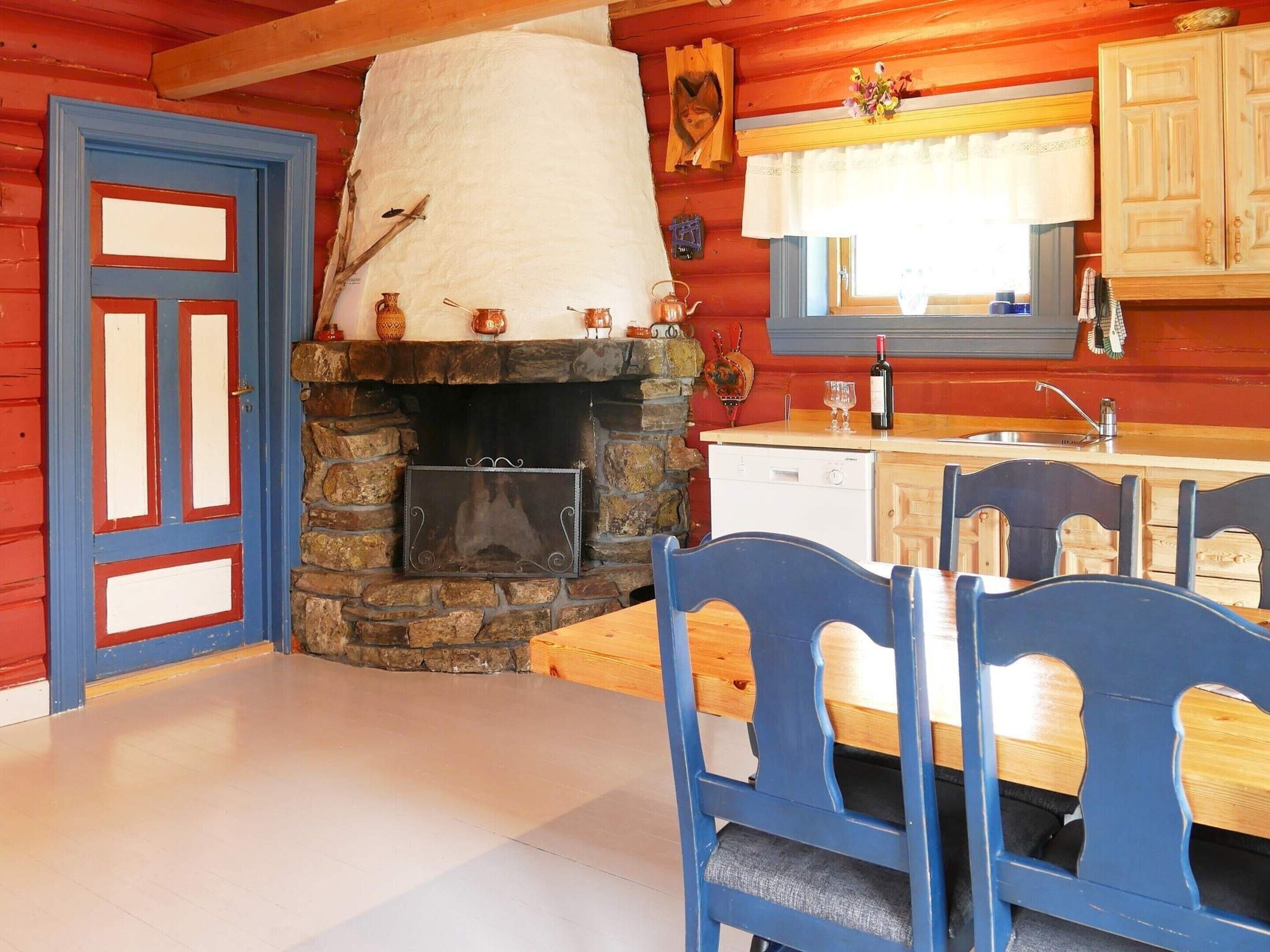 A rustic cabin interior with a stone fireplace, wooden dining table, and blue chairs.