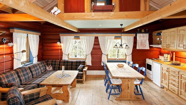 A cabin interior with a wooden dining table, blue chairs, a plaid sofa, and a kitchen area with wooden cabinets. - 5 Person Holiday Home in Hemsedal (Hemsedal)
