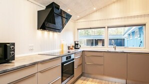 A modern kitchen with a built-in oven, a microwave, and a window overlooking a blue house. - 9 Person Holiday Home in Laeso (Læsø)