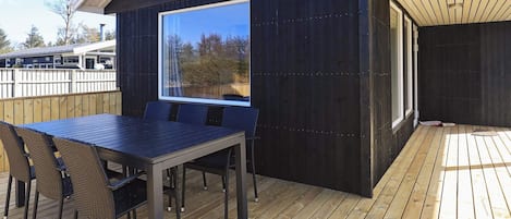 A deck with a table and chairs, a large window, and a wooden deck.