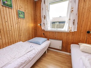 A small, cozy room with wooden walls, two single beds, a window with curtains, and a radiator. - 6 Person Holiday Home in Lokken (Lokken)