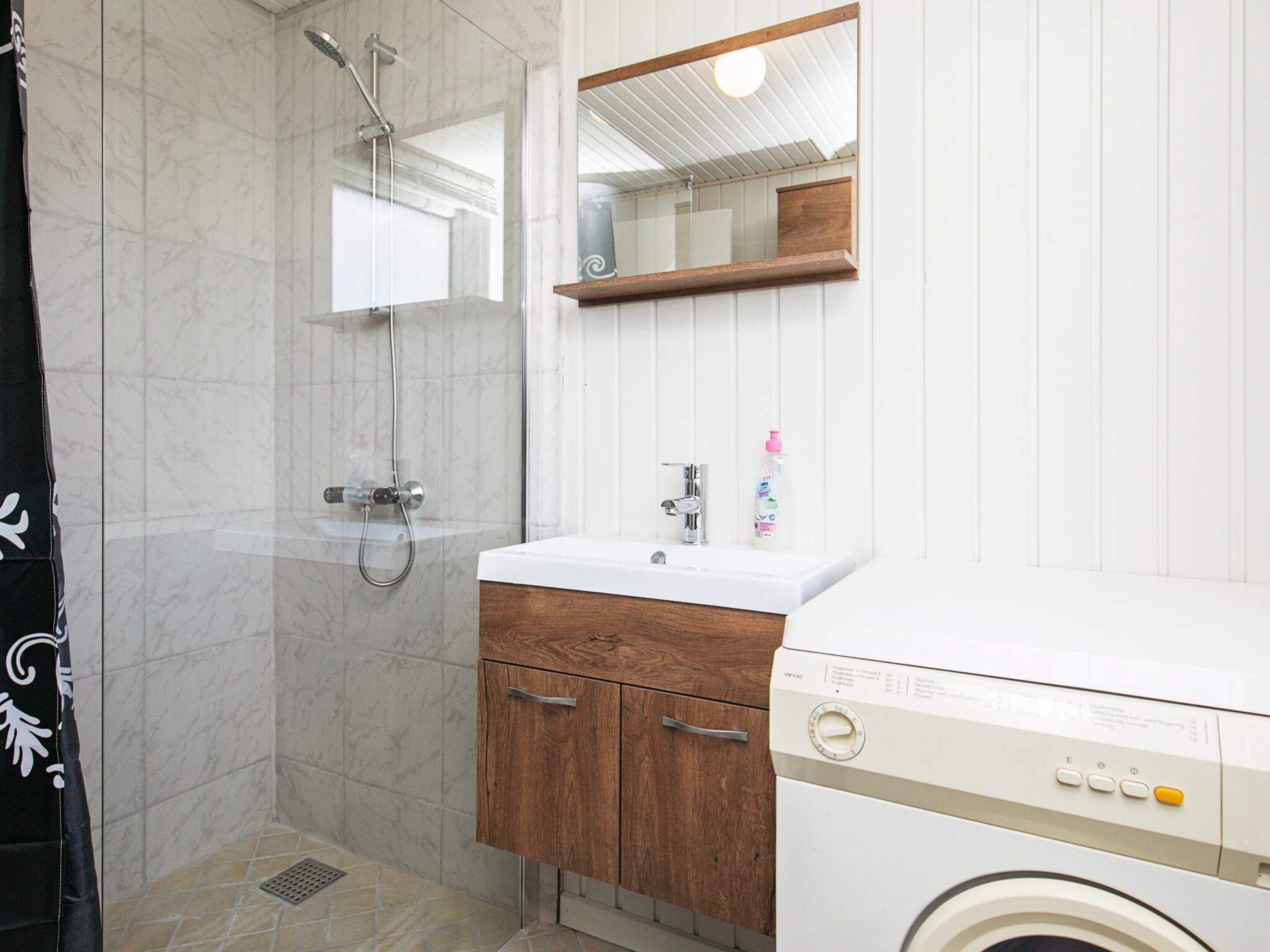 A bathroom with a shower, sink, wooden cabinet, and a washing machine.