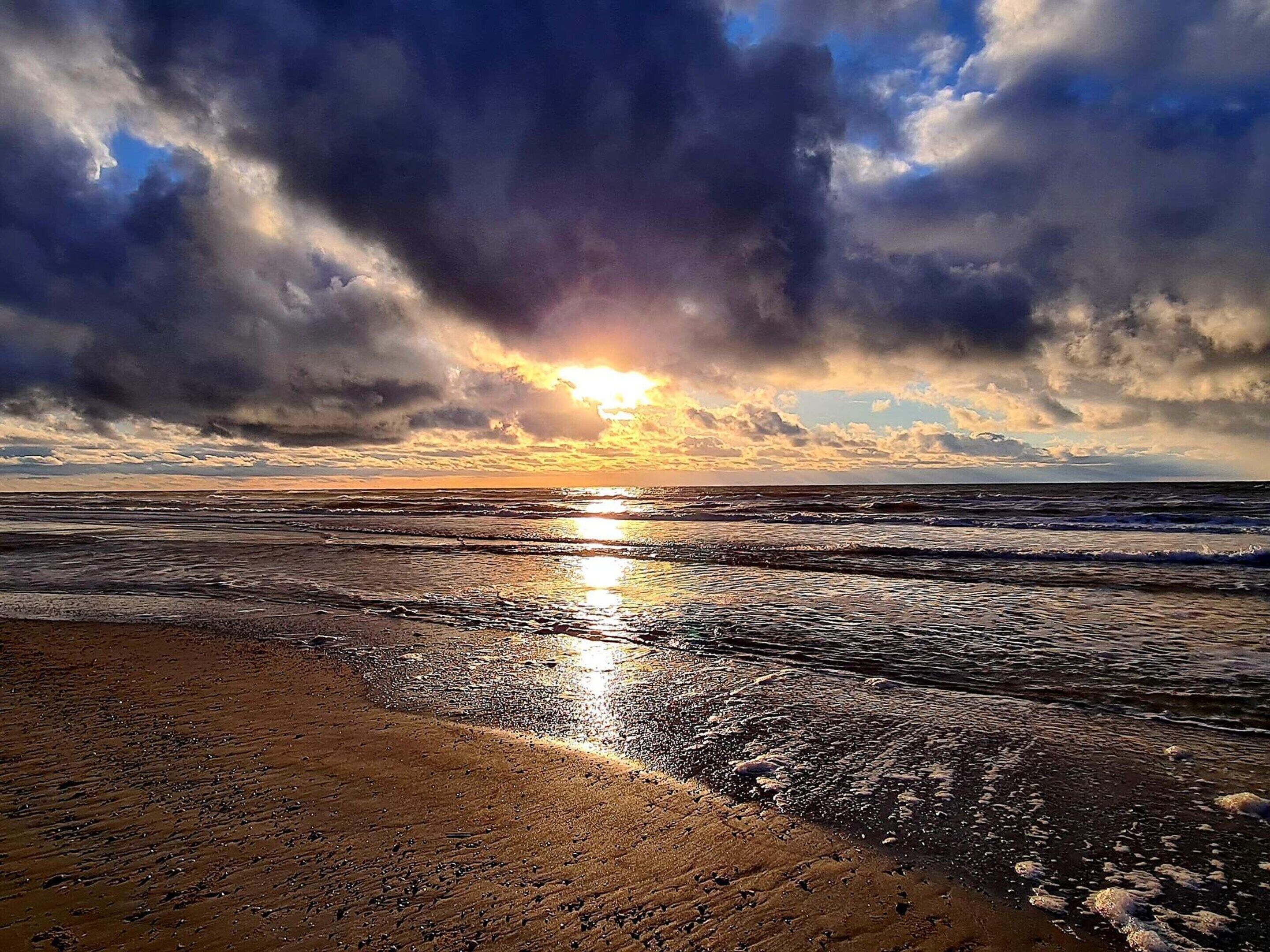 Une plage avec des vagues, un coucher de soleil et un ciel nuageux.