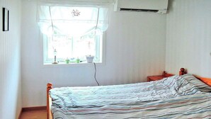 Une chambre à coucher avec un lit, une fenêtre avec des rideaux, une table de chevet et un appareil de climatisation.