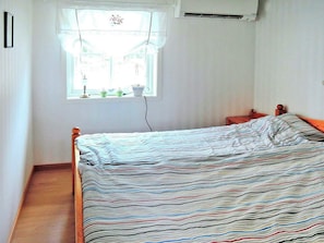 Une chambre à coucher avec un lit, une fenêtre avec des rideaux, une table de chevet et un appareil de climatisation.