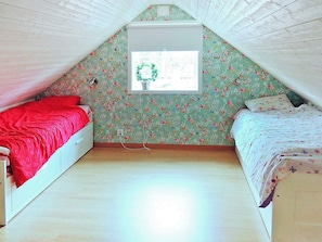 A dormitory room with two beds, floral wallpaper, a window with a wreath, and a white ceiling.