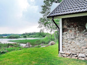 A stone building with a tiled roof, surrounded by a grassy area and a body of water.