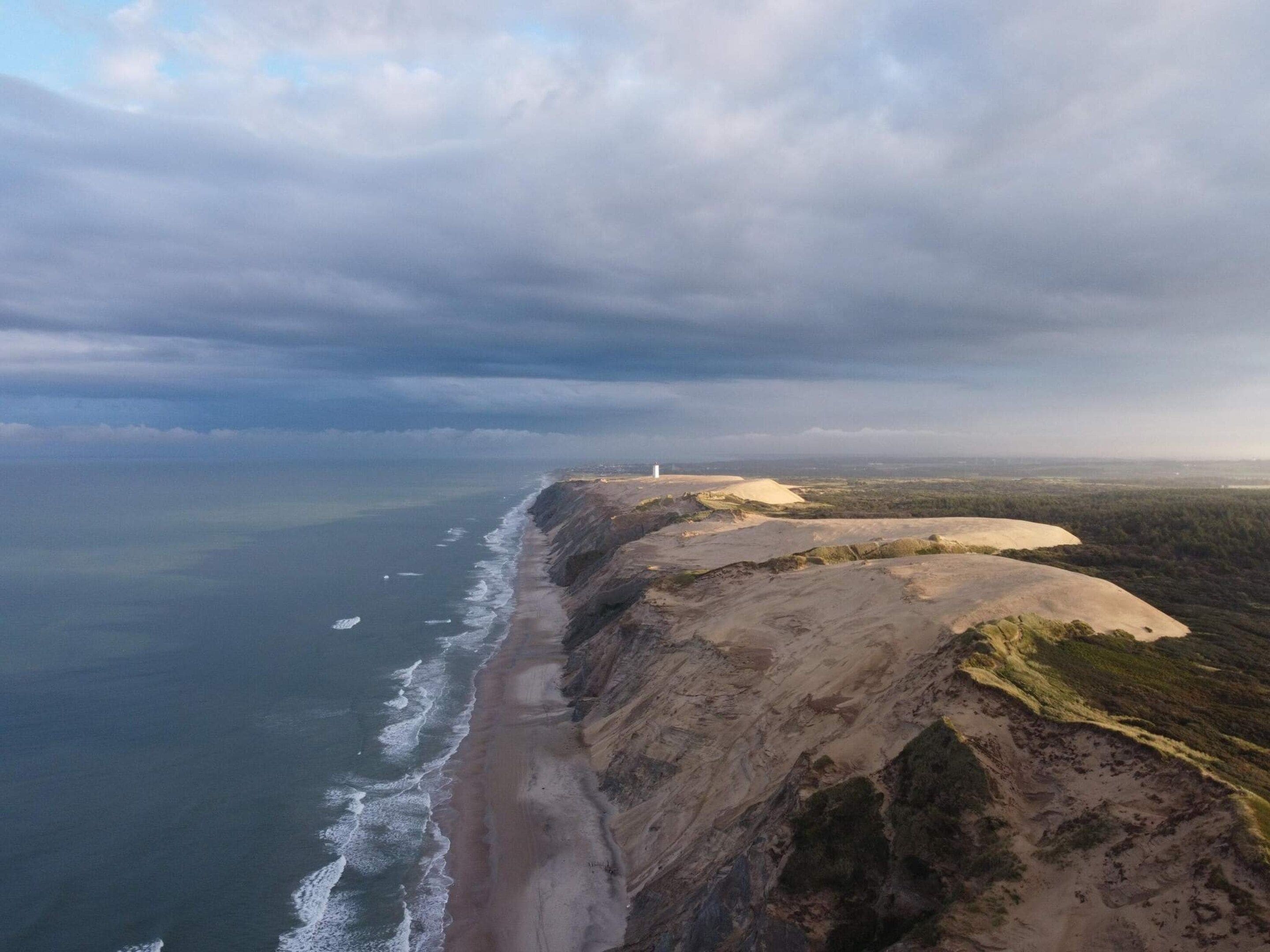 A coastal landscape with a beach, cliffs, and a lighthouse.