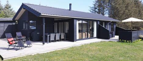 A modern house with a covered patio, outdoor seating, and a view of the surrounding landscape.