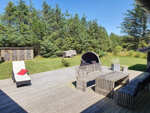 A wooden deck with outdoor furniture, a covered seating area, and a backdrop of dense trees.