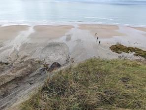 A beach with a rocky foreground and a sandy area with two people walking.