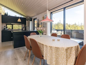 A modern kitchen with a central island, a dining area with a round table, and large windows offering a view of the outdoors.