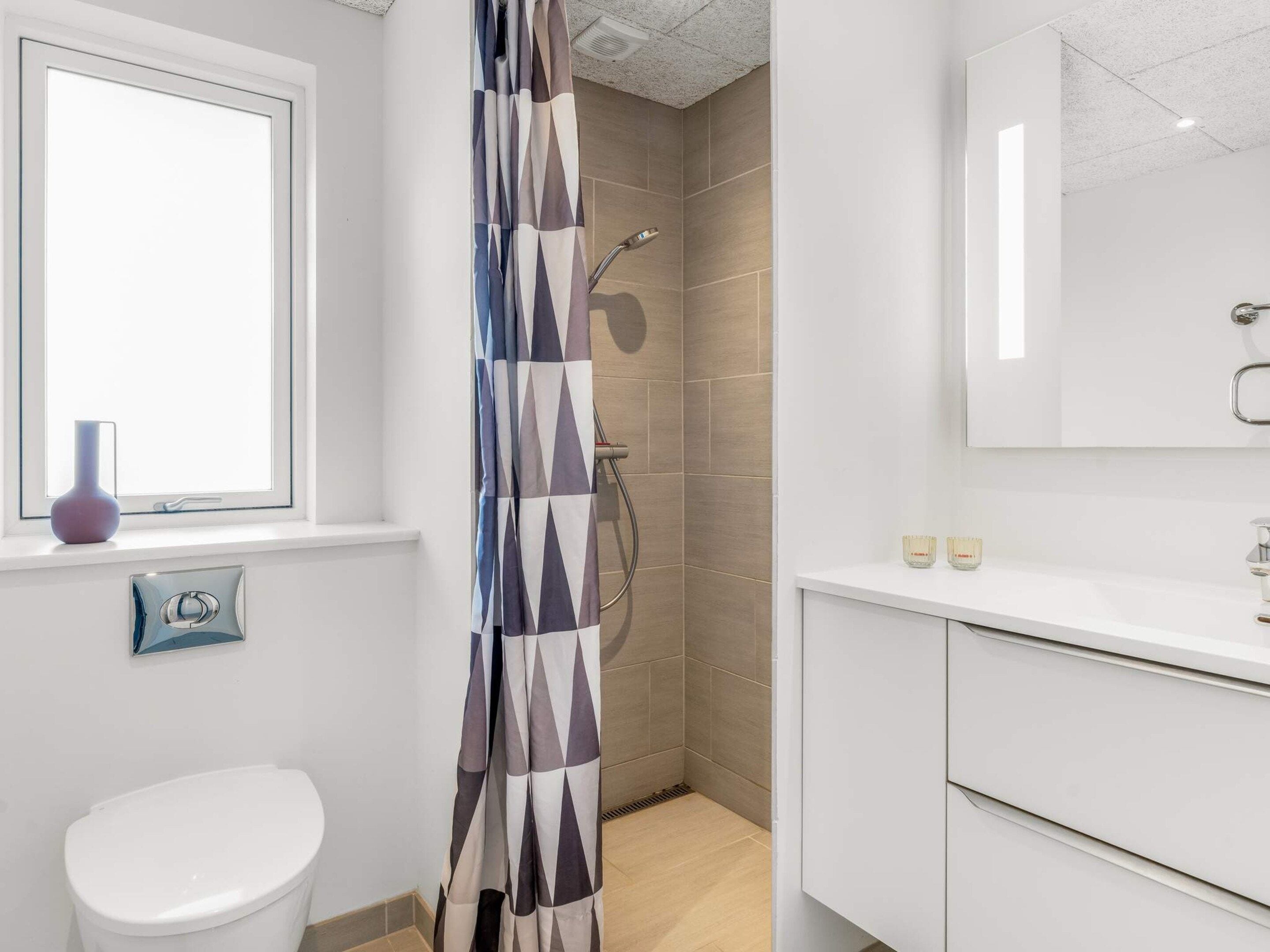 Een badkamer met een douche, toilet en een raam.